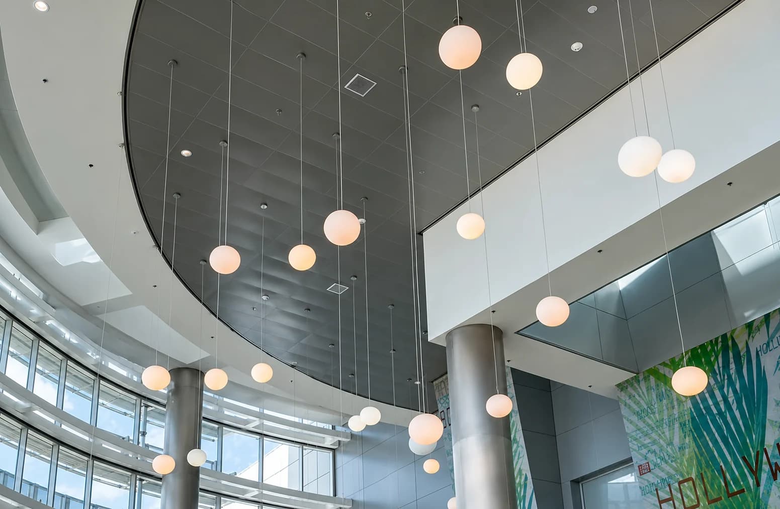 The atrium of an airport terminal: a high curved ceiling, glass walls and rows of pendant globe lights.
